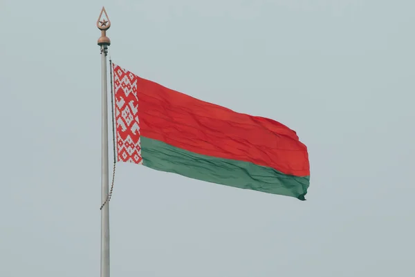 A bandeira da Bielorrússia desenvolve-se no vento contra o fundo de um céu nublado branco. Bandeira bielorrussa — Fotografia de Stock