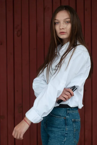 Una ragazza posa su uno sfondo rosso, una giovane modella in camicia bianca e con lunghi capelli lisci , — Foto Stock