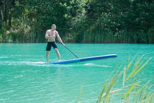 Een man met een peddel op een plank sup surfen op een meer met turquoise water — Stockfoto