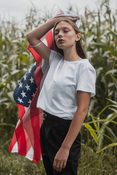 Girl with the usa flag on the background of high corn bushes, labor day concept,