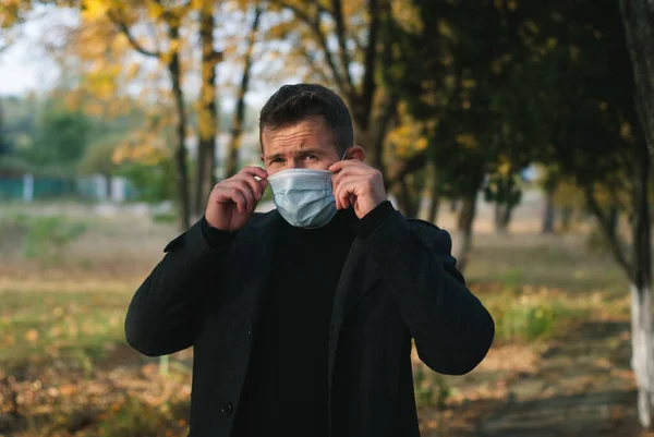 Homem Casaco Fundo Parque Outono Ajusta Uma Máscara Médica — Fotografia de Stock