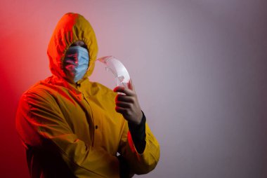 Sarı kapüşonlu bir adam güvenlik gözlüğü tutuyor.,