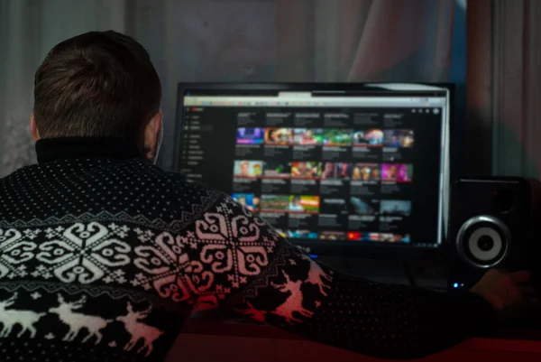 A man in a Christmas sweater watches a video on a computer — Stock Photo, Image