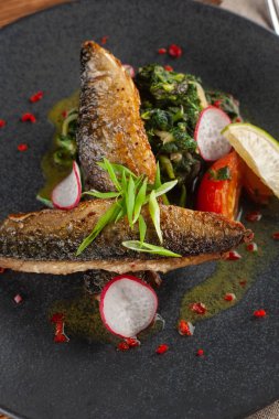 Sebze garnitür ile kızarmış uskumru balık yakın: Hindistan cevizi sütü, turp, soğan ve pişmiş domates bir moderm siyah plaka üzerinde servis ıspanak