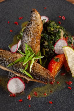 Sebze garnitür ile kızarmış uskumru balık yakın: Hindistan cevizi sütü, turp, soğan ve pişmiş domates bir moderm siyah plaka üzerinde servis ıspanak