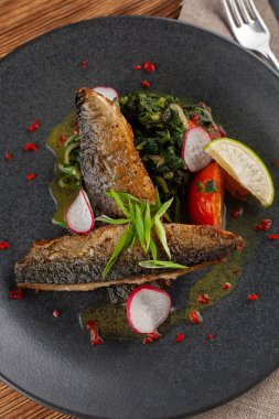 Sebze garnitür ile kızarmış Uskumru balığı: Hindistan cevizi sütü, turp, soğan ve pişmiş domates bir moderm siyah plaka üzerinde servis ıspanak