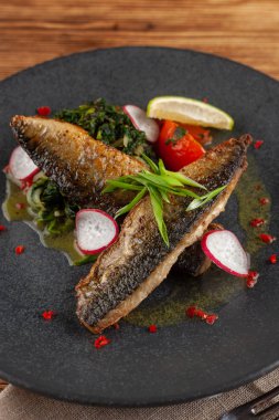 Sebze garnitür ile kavrulmuş uskumru balık ağız sulandıran: Hindistan cevizi sütü, turp, soğan ve pişmiş domates bir moderm siyah plaka üzerinde servis ıspanak