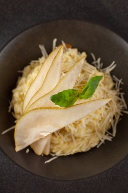 Modern siyah plaka üzerinde hizmet tavuk suyu, rendelenmiş parmesan, fesleğen ve dilimlenmiş olgun armut ile geleneksel İtalyan risotto yakın