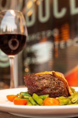 Yeşil fasulye ve taze kiraz domates ile kavrulmuş Orta nadir Mignon fileto, krem sos ile dekore bir terasta kırmızı şarap bir bardak ile servis