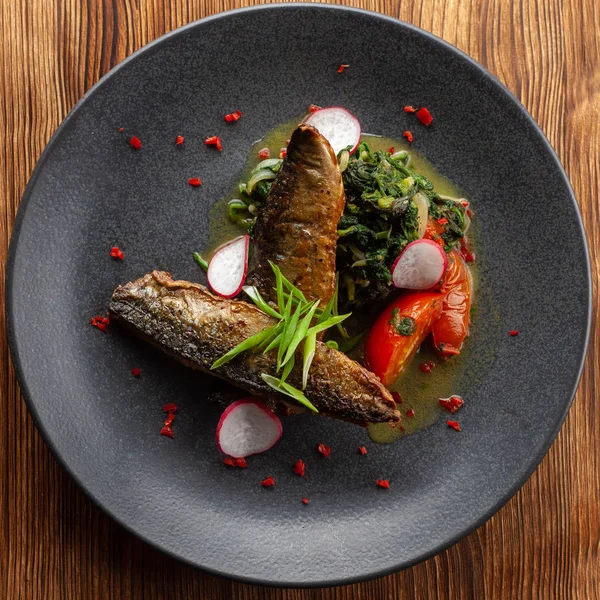 Gebratener Makrelenfisch mit Gemüsegarnitur: Spinat in Kokosmilch, Rettich, Zwiebeln und gebackenen Tomaten auf einem moderaten schwarzen Teller serviert — Stockfoto