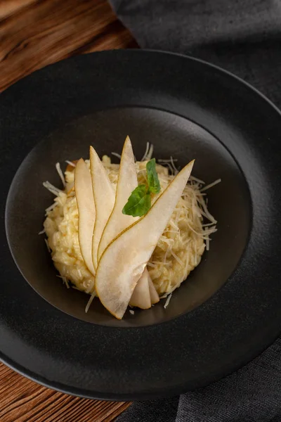 Risotto al tartufo cremoso con parmigiano grattugiato, basilico e pera matura affettata, servito su un tavolo di legno — Foto Stock