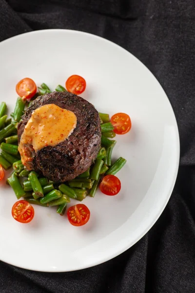 Vista de perto de um bife mignon raro médio, assado com feijão verde e tomate cereja fresco, decorado com molho cremoso — Fotografia de Stock