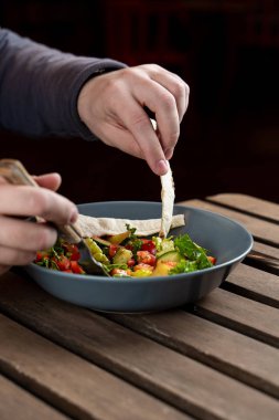 Genç adam pişmiş ceket patates ile sıcak mevsimlik salata ile hafif bir yemek yiyor, düz ekmek ile servis