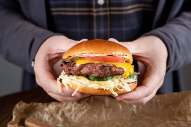 Genç adam çedar peyniri ve sığır köftesi ile sulu bir cheeseburger tutuyor