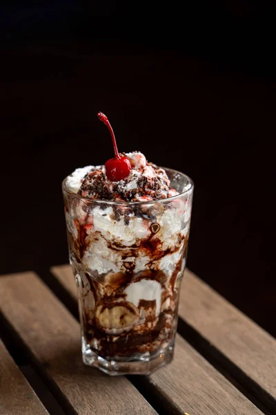 Sobremesa de sorvete em camadas com chantilly, molho de chocolate e sorvete de baunilha no terraço de verão com luzes no fundo — Fotografia de Stock