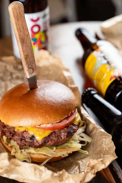 Juicy cheeseburger with melted cheese and fat beef patty with knife in it served with cold beer