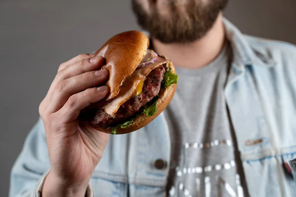 Genç sakallı adam buz gibi bira ile gevrek pastırma ile sulu bir hamburger yiyor