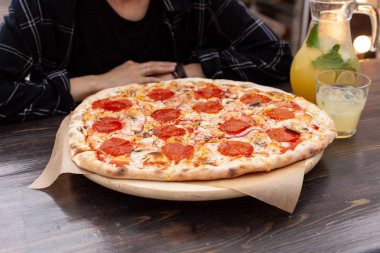Genç Avrupalı kadın eritilmiş peynir ve narenciye limonata ile İtalyan pepperoni pizza yiyor