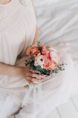 Gelin beyaz bir yatakta elinde pembe bir buketle oturuyor.