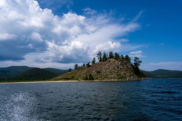 Russia, Irkutsk region, Baikal lake, July 2020: small yellow sand island with rare trees, from water view