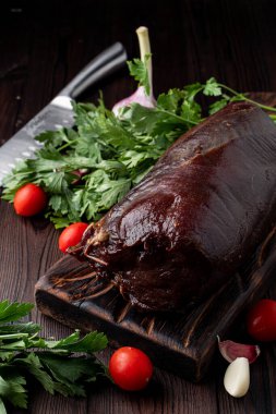 Kanlı fileto, koyu ahşap bir masanın üzerinde. Etrafında otlar var.