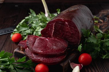 Çiğ fileto, dilimlenmiş ve otlarla çevrili, koyu arka planda, bir pazar kataloğu için fotoğraf