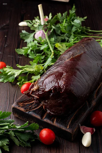 Kanlı fileto, koyu ahşap bir masanın üzerinde. Etrafında otlar var.
