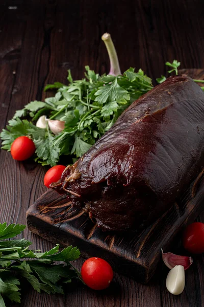 Kanlı fileto, koyu ahşap bir masanın üzerinde. Etrafında otlar var.