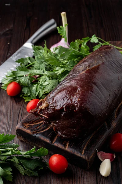 Kanlı fileto, koyu ahşap bir masanın üzerinde. Etrafında otlar var.
