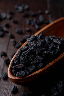 Siyah kuru üzümleri ahşap bir kasede yakın plan, karanlık arka plan, yumuşak ışıklı stüdyo fotoğrafı.
