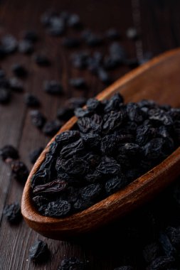 Siyah kuru üzümleri ahşap bir kasede yakın plan, karanlık arka plan, yumuşak ışıklı stüdyo fotoğrafı.