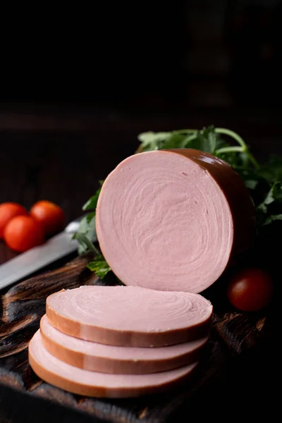 Pink bologna, sliced in thick pieces on dark background, magazine photo