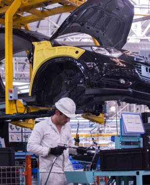 İş yerindeki erkekler. Koruyucu şeyler giyen genç bir adam, bir araba fabrikasında alet ve makinelerle çalışıyor.