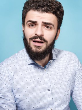Bir sürpriz, empatik yüz ve açık ağzı olan genç bir adam portresi. Şık görünümü, bıyık ve sakal. Tarafsız mavi arka plan