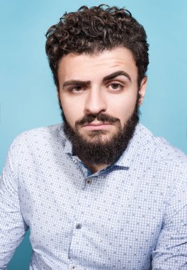 Mavi bir arka plan üzerinde bakışları olan genç bir adam portresi. Şık görünümü, bıyık ve sakal