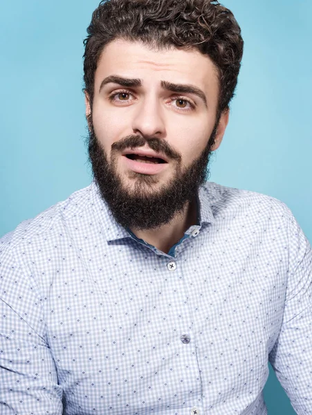 Bir sürpriz, empatik yüz ve açık ağzı olan genç bir adam portresi. Şık görünümü, bıyık ve sakal. Tarafsız mavi arka plan