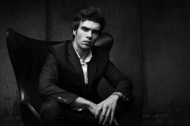 Şık genç adam bir sandalyede oturuyor. Siyah ceket ve beyaz gömlek. Siyah-beyaz karakteristik portre