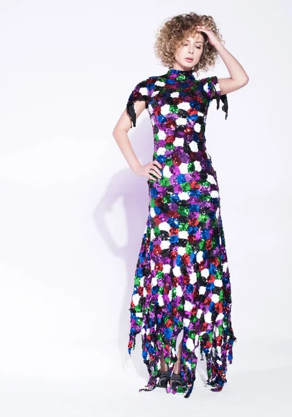 Renkli uzun elbiseli bir genç kadın. Bir el saçları ile çalışır. Hacimli saç bukleler. Tarafsız beyaz arka plan