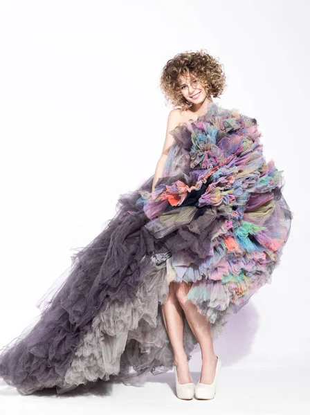 Bir hacimli beyaz bir duvar önünde poz içinde neşeli genç kadın. Saç modeli bukleler ve parlak bir gülümseme ile