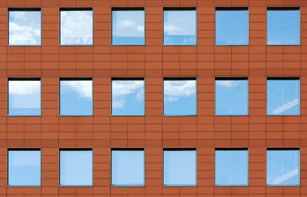 Minimalist facade of modern office building with square Windows. Finish is a dark red color. The details of the architecture of the urban landscape