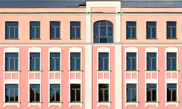 The facade of the old building with pink walls and white decor on the windows. Upper floors, roof and sky