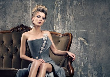 Parti zamanı üzüntü. Gri Abiye vintage kanepede oturan yalnız güzel genç kadın. İnce rakam, ihale bak. Saç ve makyaj. Arka plan beton duvar