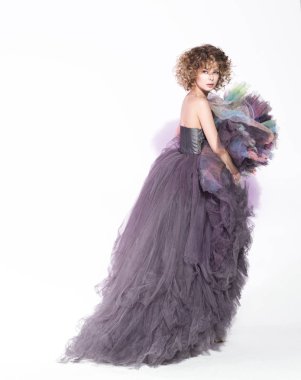 Duvardaki beyaz arka plan üzerinde uzun gri elbiseli poz genç güzel kadın. Şık saç modeli, bir göz geri