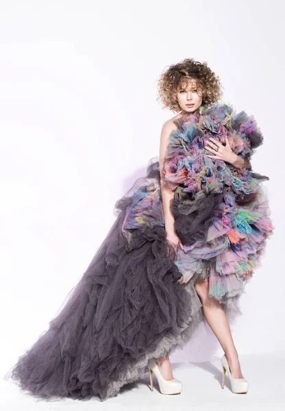 Renkli elbiseyle poz güzel ve genç birbayan. Kıvırcık saçları ve şehvetli bak. Tarafsız beyaz arka plan boş alan ile