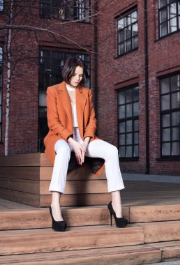 Kırmızı ceket ve beyaz pantolon ahşap bir bankta oturan bir genç kadın. Sokak moda portre. İş kentsel tarzı