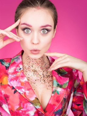 Renkli stüdyo gözleri açık olan güzel bir kadın portresi. Çok şaşırdım bak. Makyaj glitter ile. Tasvir ve eller gesticulating. Pembe bir arka plan