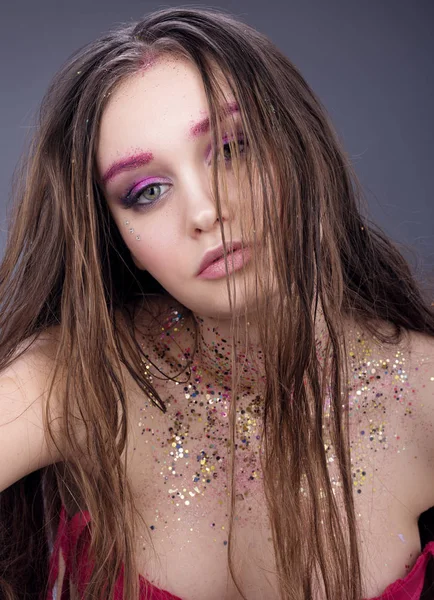 Portrait of sexy young woman with wet hair. Neutral face makeup with glitter. Dark gray background