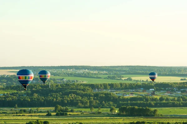 Flying in a balloon. Three objects in the air. Green fields and forests. Clear sky