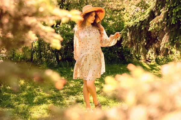 Молодая красивая женщина танцует в парке. Шляпа и светлое летнее платье — стоковое фото
