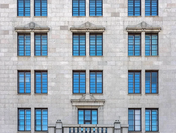 Die Fassade des Stadtgebäudes mit grauem Stein. die Fenster spiegeln den blauen Himmel wider — Stockfoto